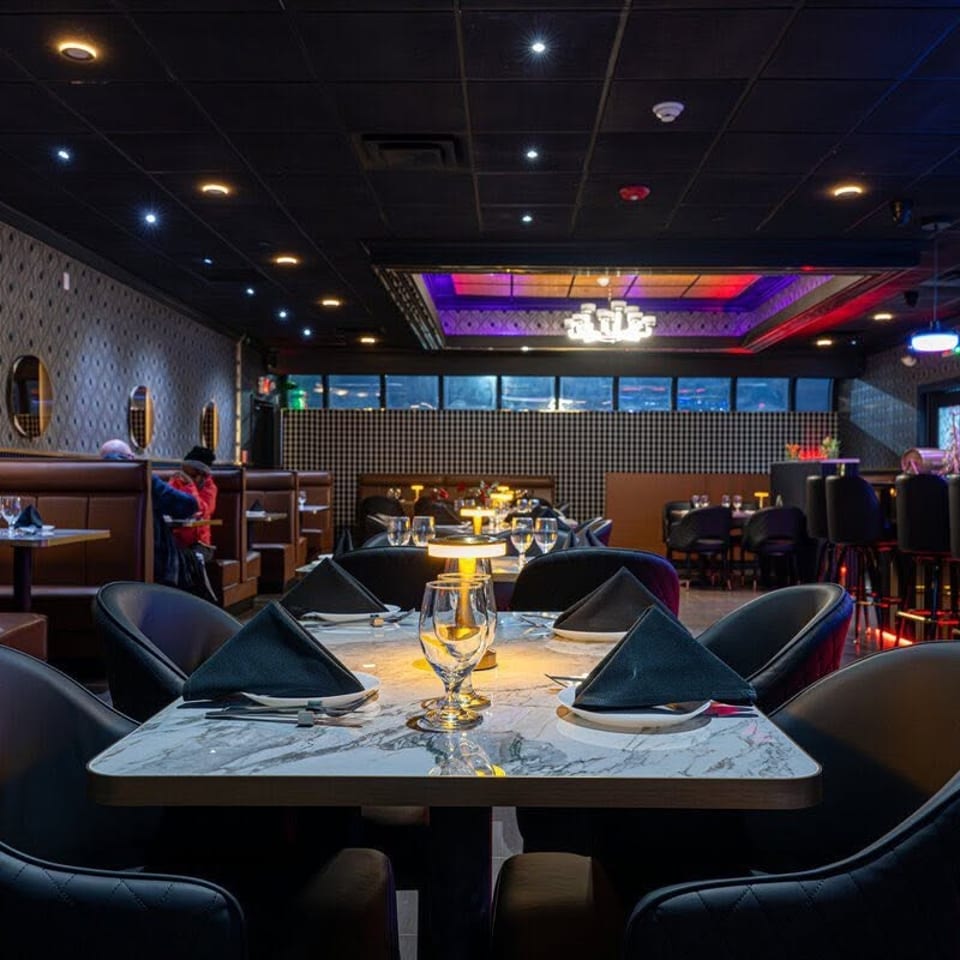 Upscale restaurant interior with marble tables, black napkins, leather seating, patterned walls, and colorful ambient lighting.