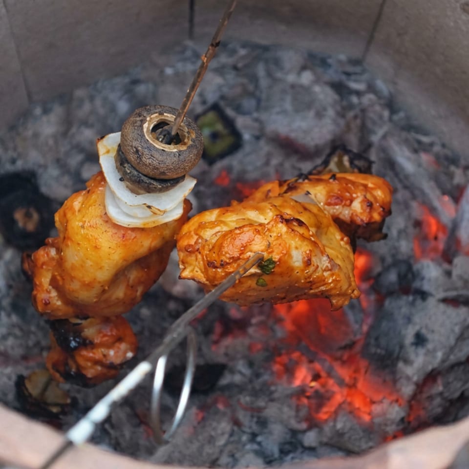 Marinated chicken pieces roast on skewers over glowing charcoal inside a clay tandoor oven.