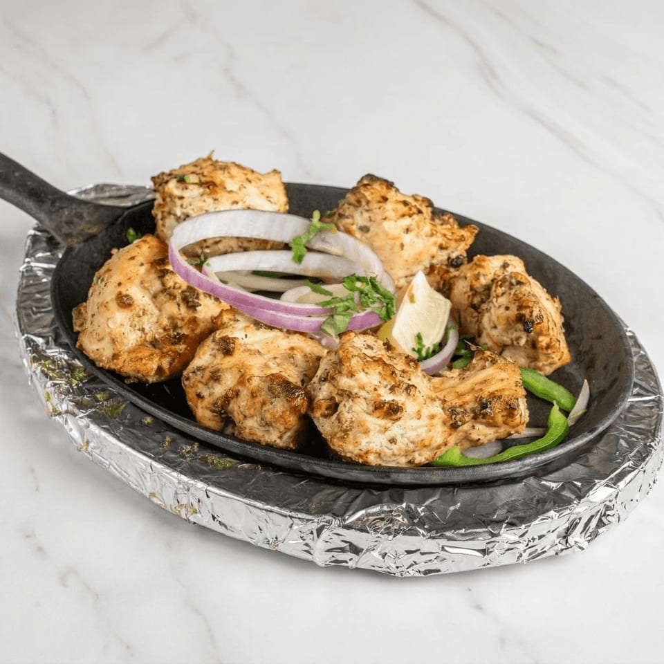 Grilled chicken kebabs garnished with red onion, herbs, lemon, and green peppers on a cast-iron platter.